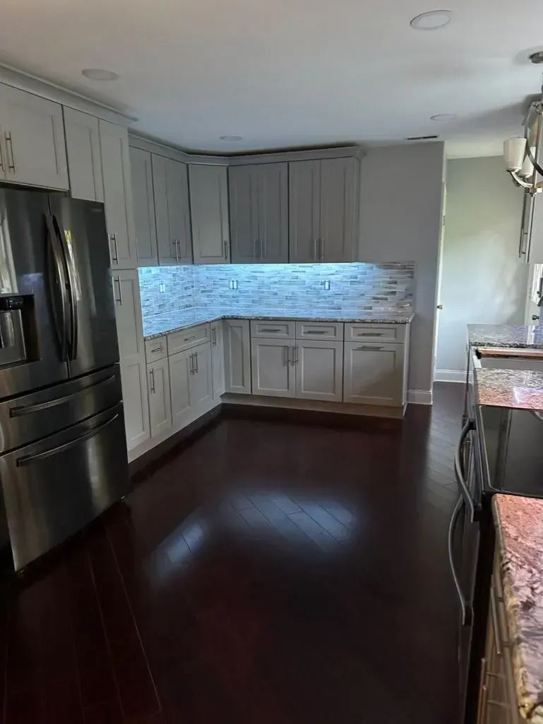 Modern kitchen with dark wood floors, white cabinets, stainless steel fridge, and blue tile backsplash