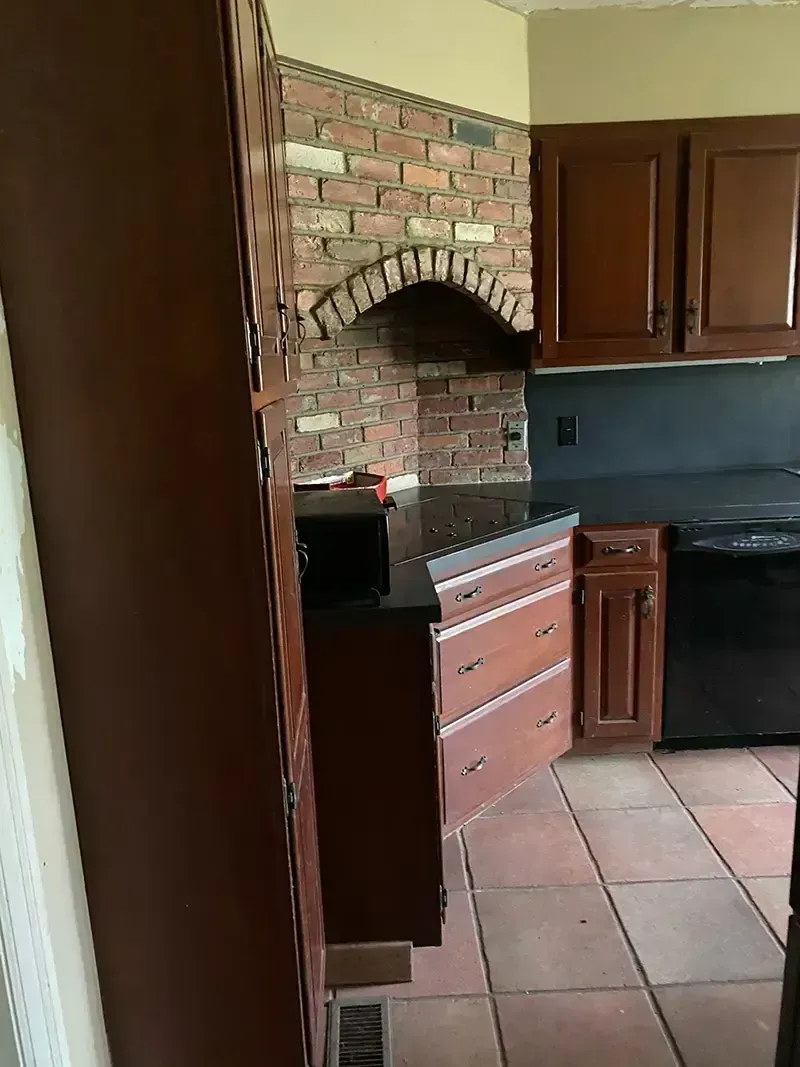 Kitchen with brick arch above stove, wooden cabinets, black countertop, and terracotta tile floor.