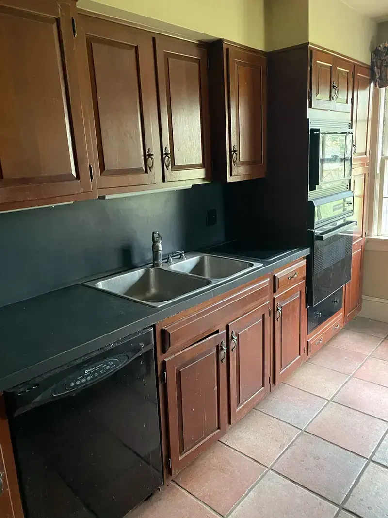 Small kitchen with dark wood cabinets, black countertops, stainless sink, and a windowed door.