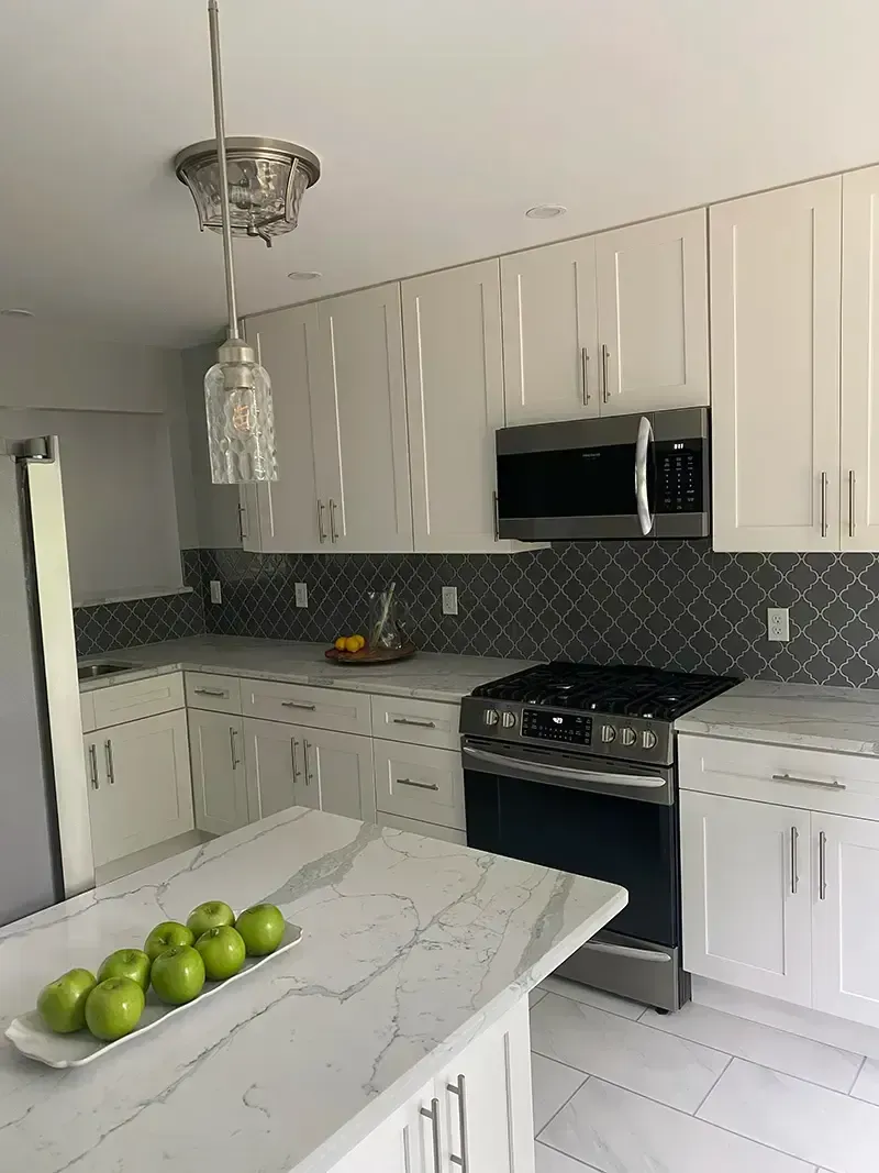 Modern white kitchen with marble island, stainless stove, and green apples in a bowl