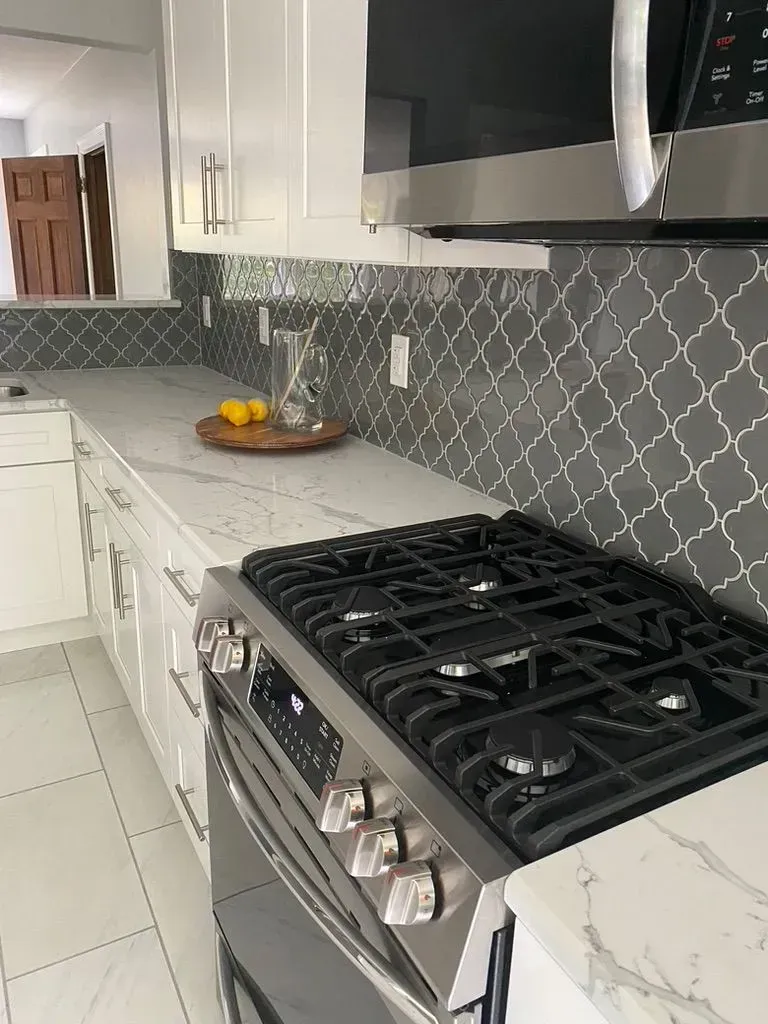 Modern kitchen with white cabinets, black stove, marble countertops, and gray patterned backsplash.