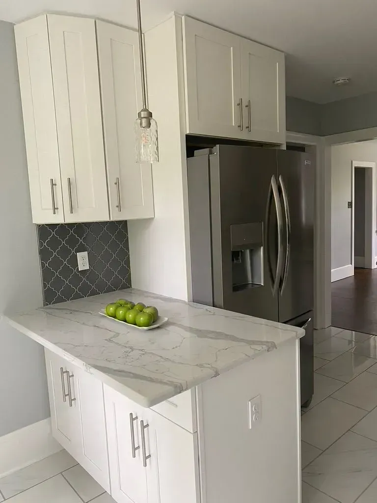 Bright kitchen with white cabinets, marble island, stainless fridge, and a bowl of green apples.