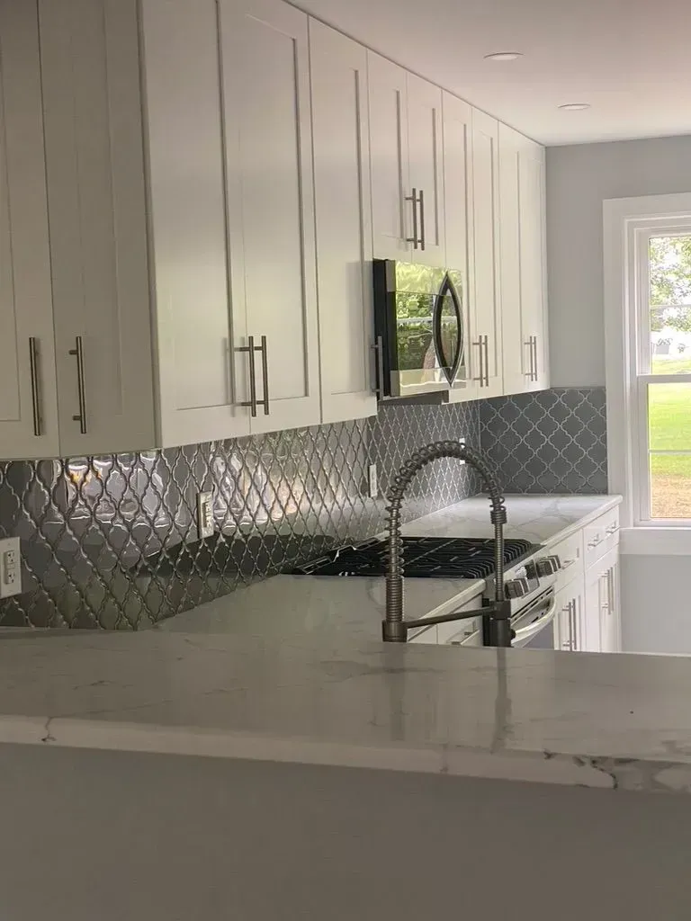 Modern white kitchen with gray tile backsplash, marble countertop, and sink near a window