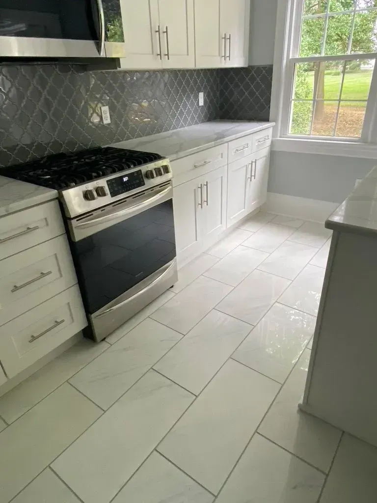 Bright white kitchen with stainless steel stove, white cabinets, and large window by the counter.