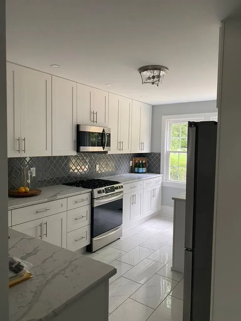 Bright white modern kitchen with stainless steel appliances, tiled backsplash, and a windowed doorway.
