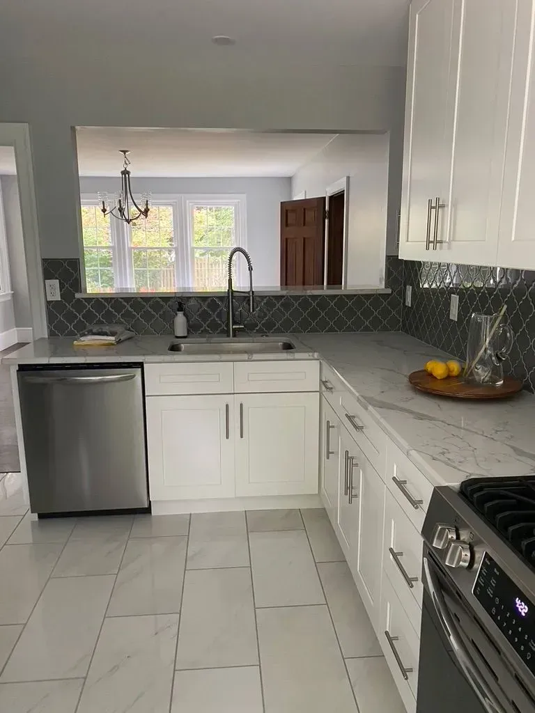 Bright white kitchen with stainless steel appliances, dark backsplash, and a view into the dining area.