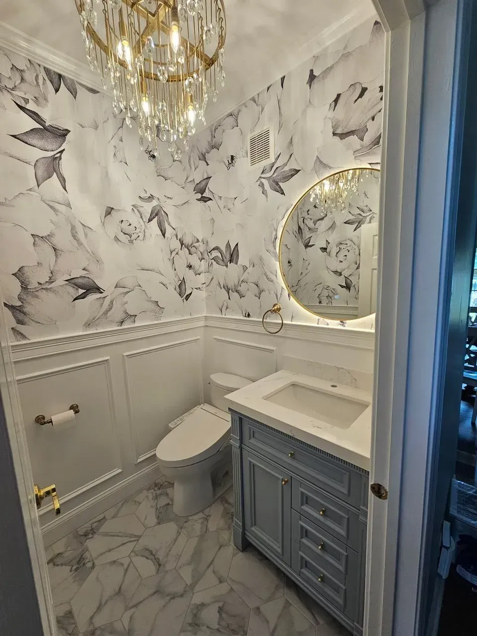 Elegant marble-patterned bathroom with toilet, vanity, round mirror, and gold chandelier