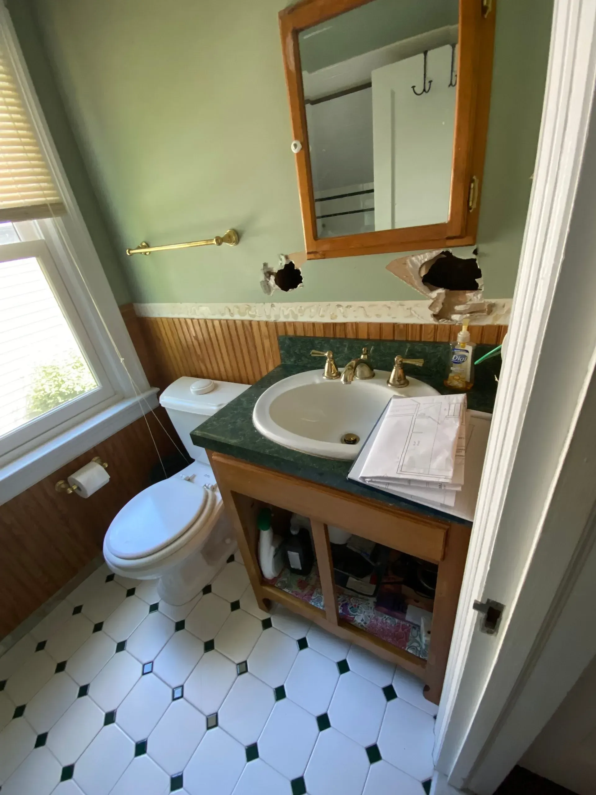 Small bathroom with white toilet, green countertop sink, wooden mirror, and black-and-white tiled floor.