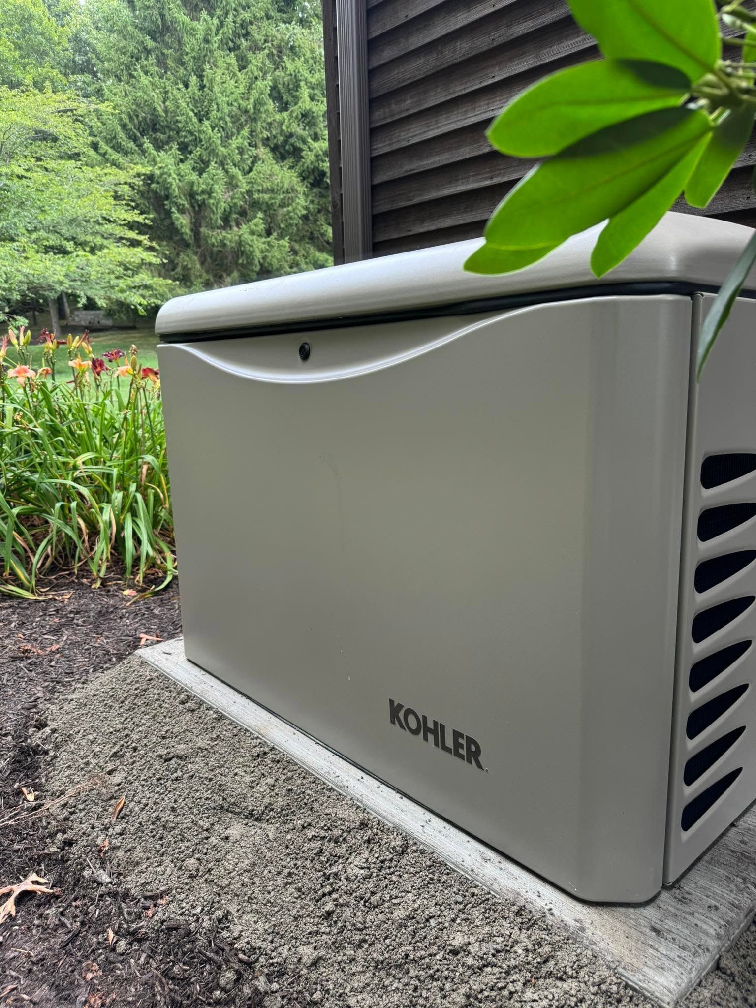 KOHLER outdoor generator enclosure beside a house with gravel and greenery