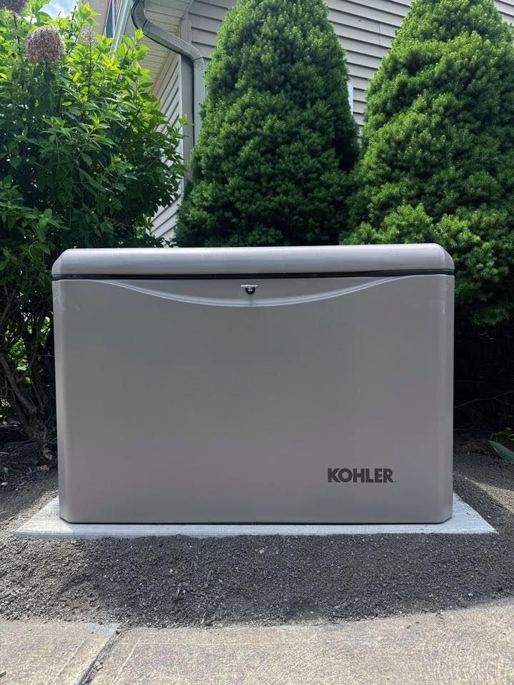 Gray Kohler generator on a concrete pad beside a house and shrubs