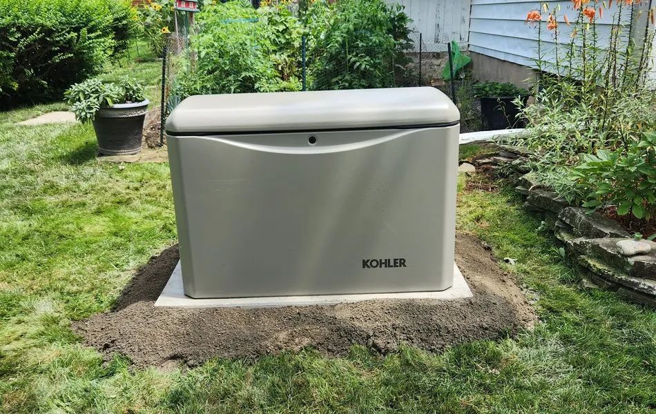 Gray outdoor storage box in a garden, sitting on a small gravel base amid grass and plants.