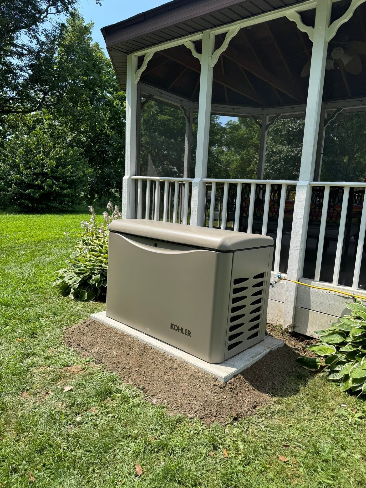 Beige outdoor backup generator beside a white porch in a grassy yard.