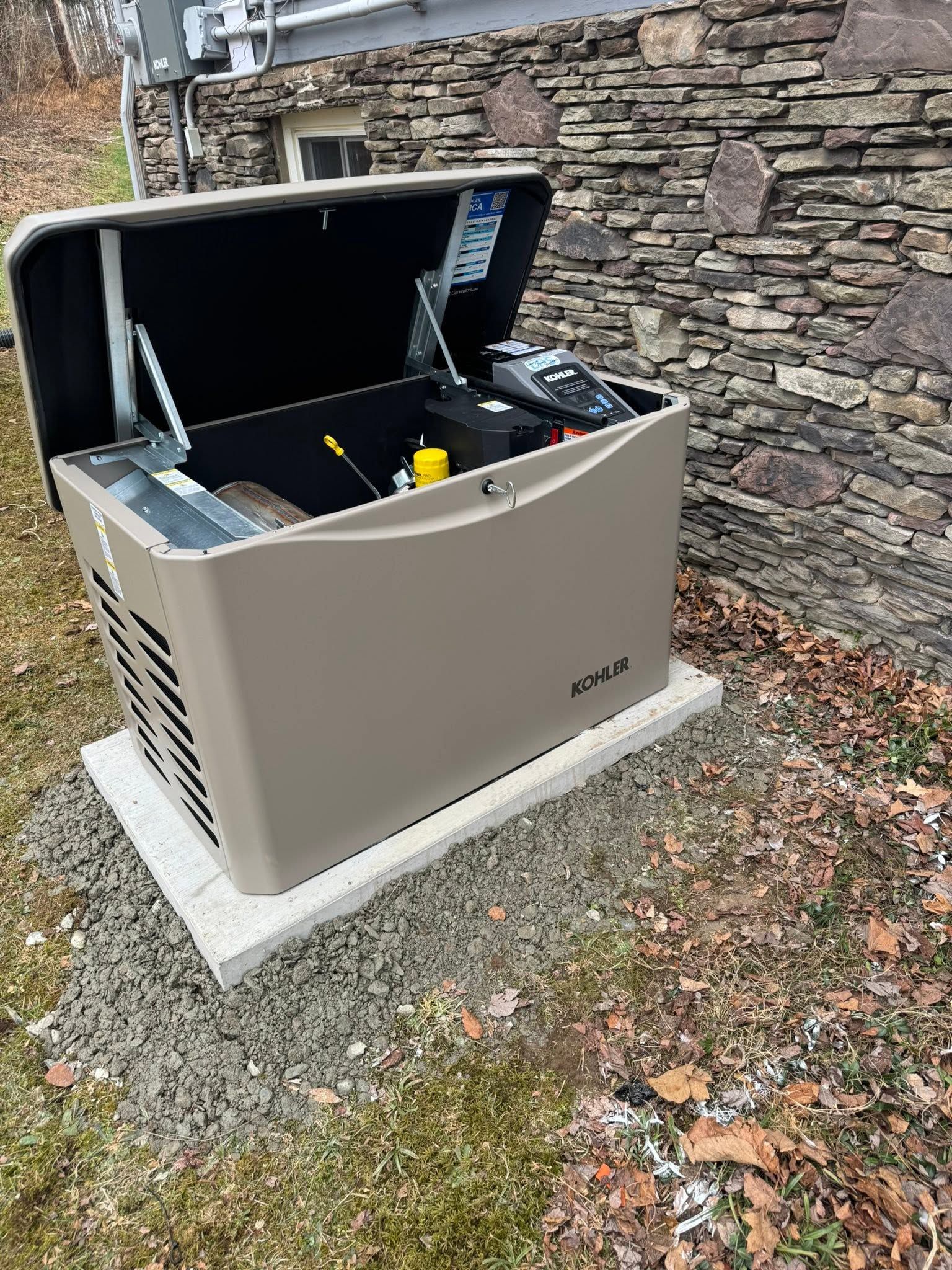Outdoor beige generator with open lid beside a stone wall on a concrete pad.
