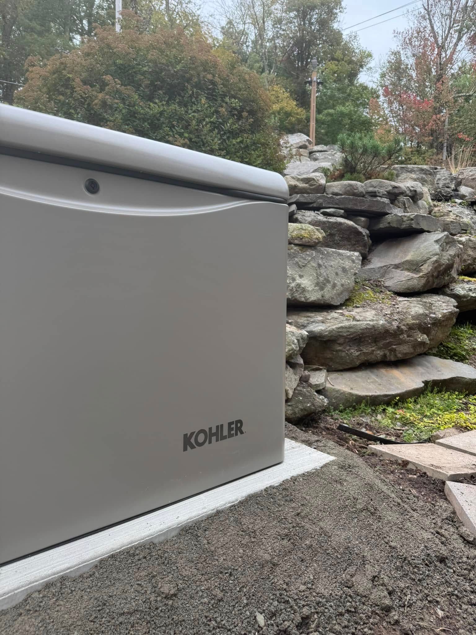 Kohler generator beside a stone retaining wall outdoors on a gravel surface