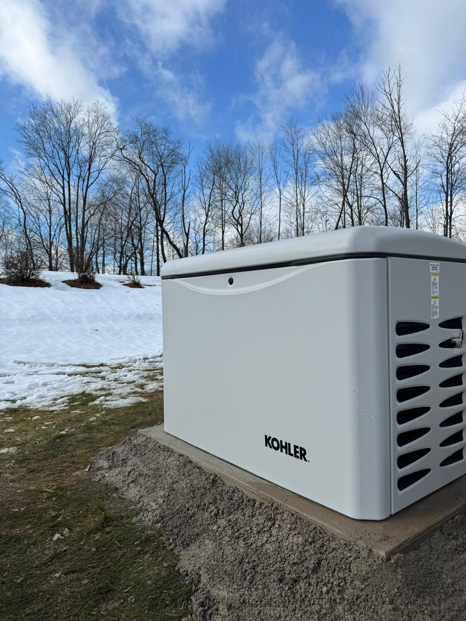 White generator on a snowy yard with bare trees and blue sky in the background
