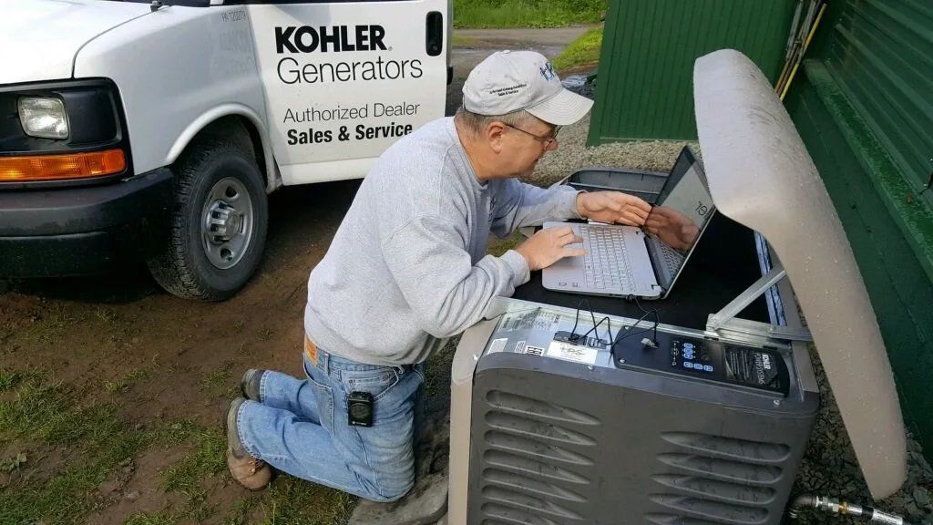Technician kneels beside an open outdoor HVAC unit, inspecting wiring near a service van.