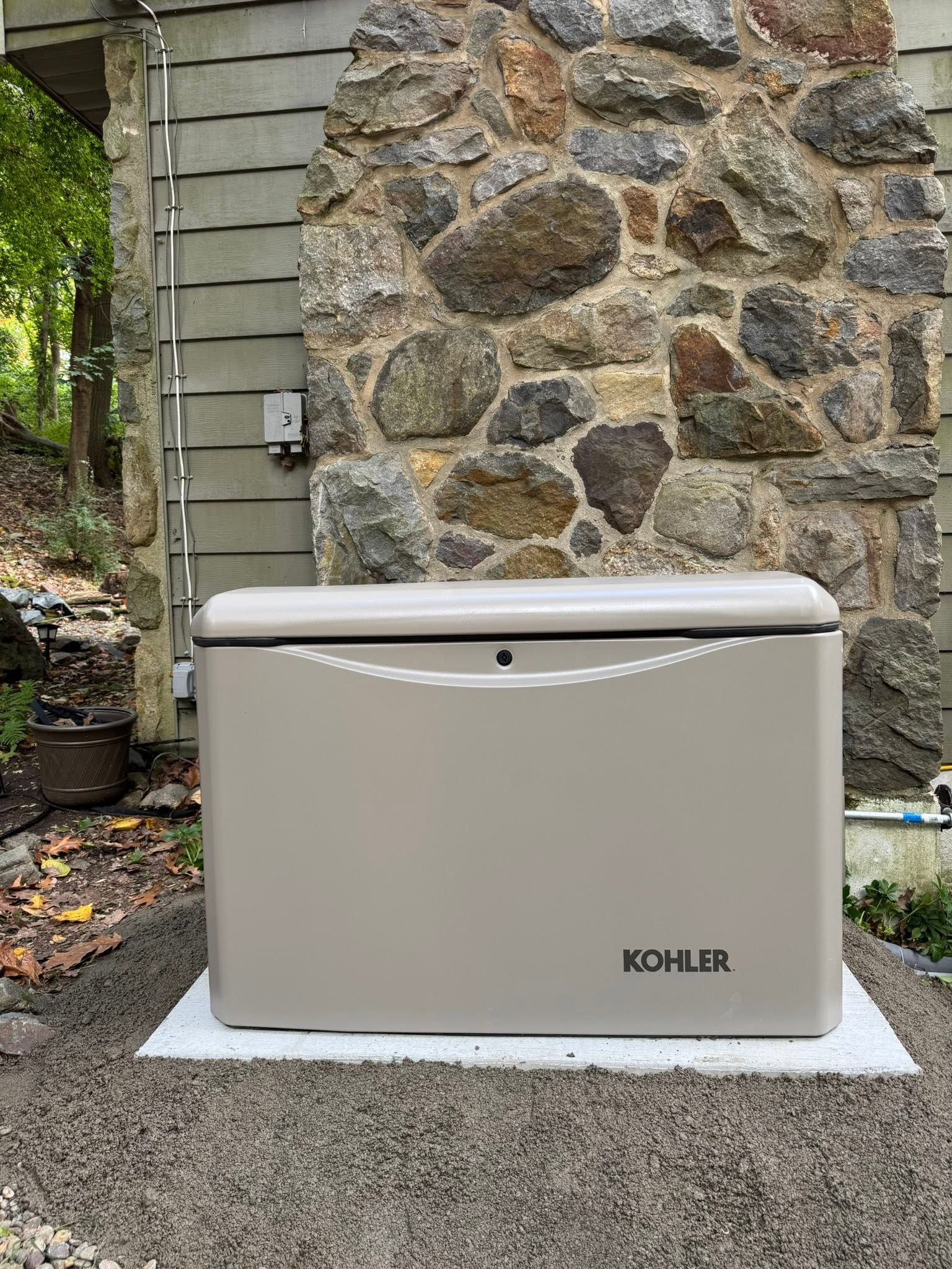 Beige Kohler backup generator outside by a stone wall and house siding
