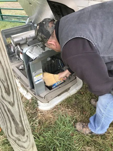Person repairing an outdoor HVAC unit beside a house, with the cover open and tools visible.
