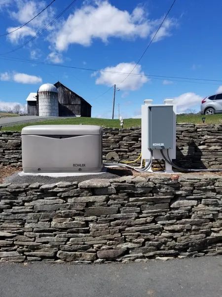 Stone wall with utility boxes and a white tank in front of a barn under a blue sky