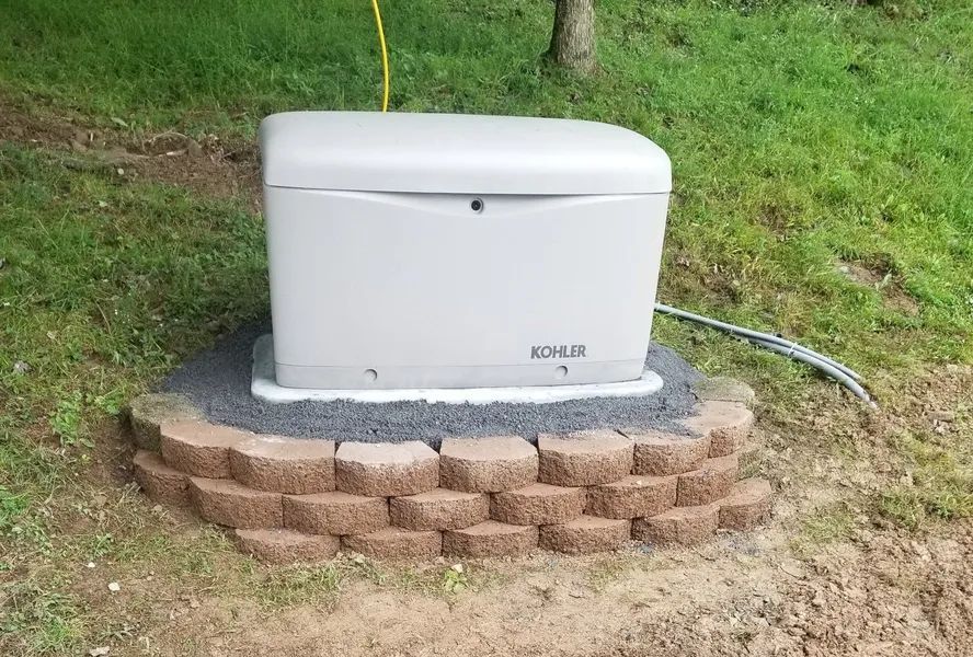 White generator on a concrete pad beside a brick retaining wall in a grassy yard