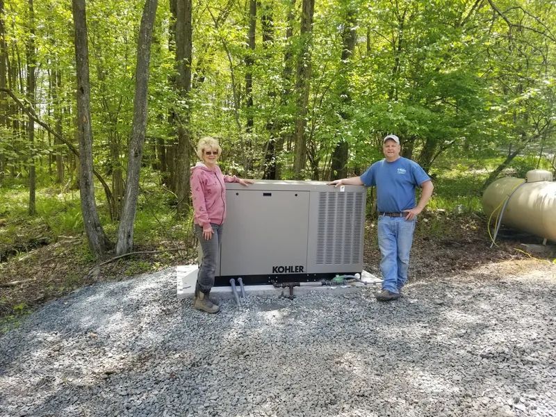 Two people standing beside a large gray outdoor generator in a wooded area