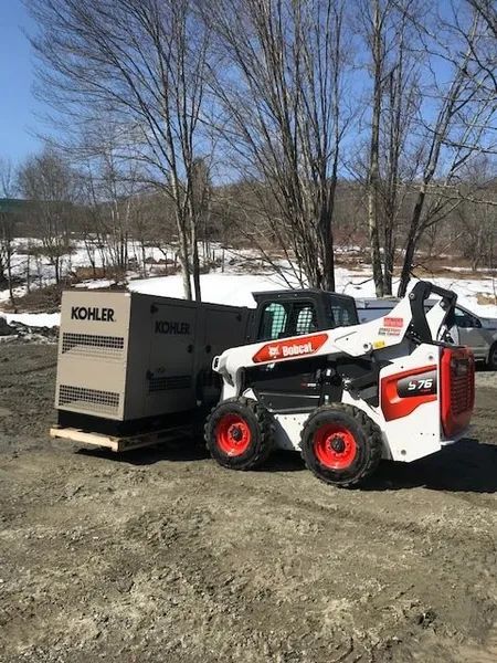 White Bobcat skid-steer parked beside a KOHLER generator on a snowy dirt lot.