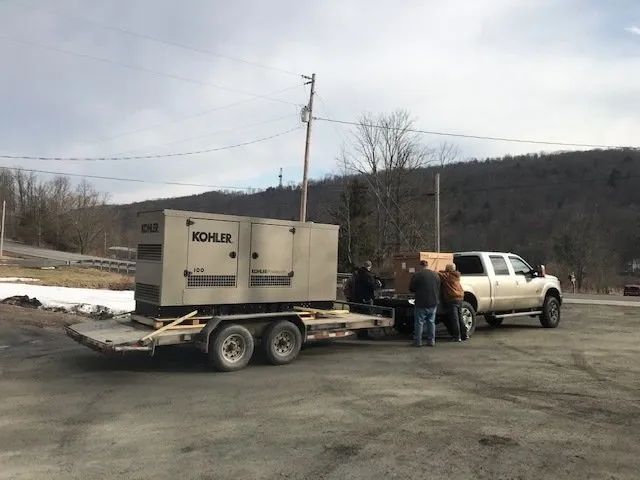 Pickup truck towing a trailer with a generator; two people stand beside it on a rural roadside.