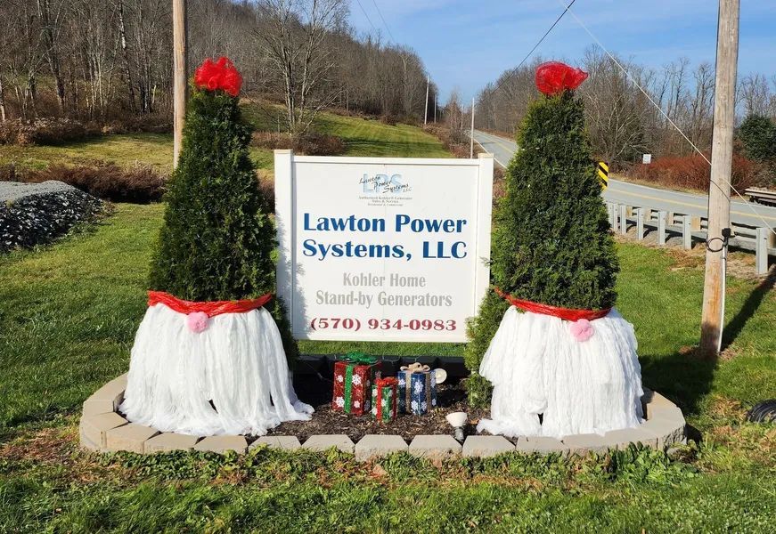 Lawn Power Systems LLC sign flanked by two decorated shrubs with red bows by a roadside.