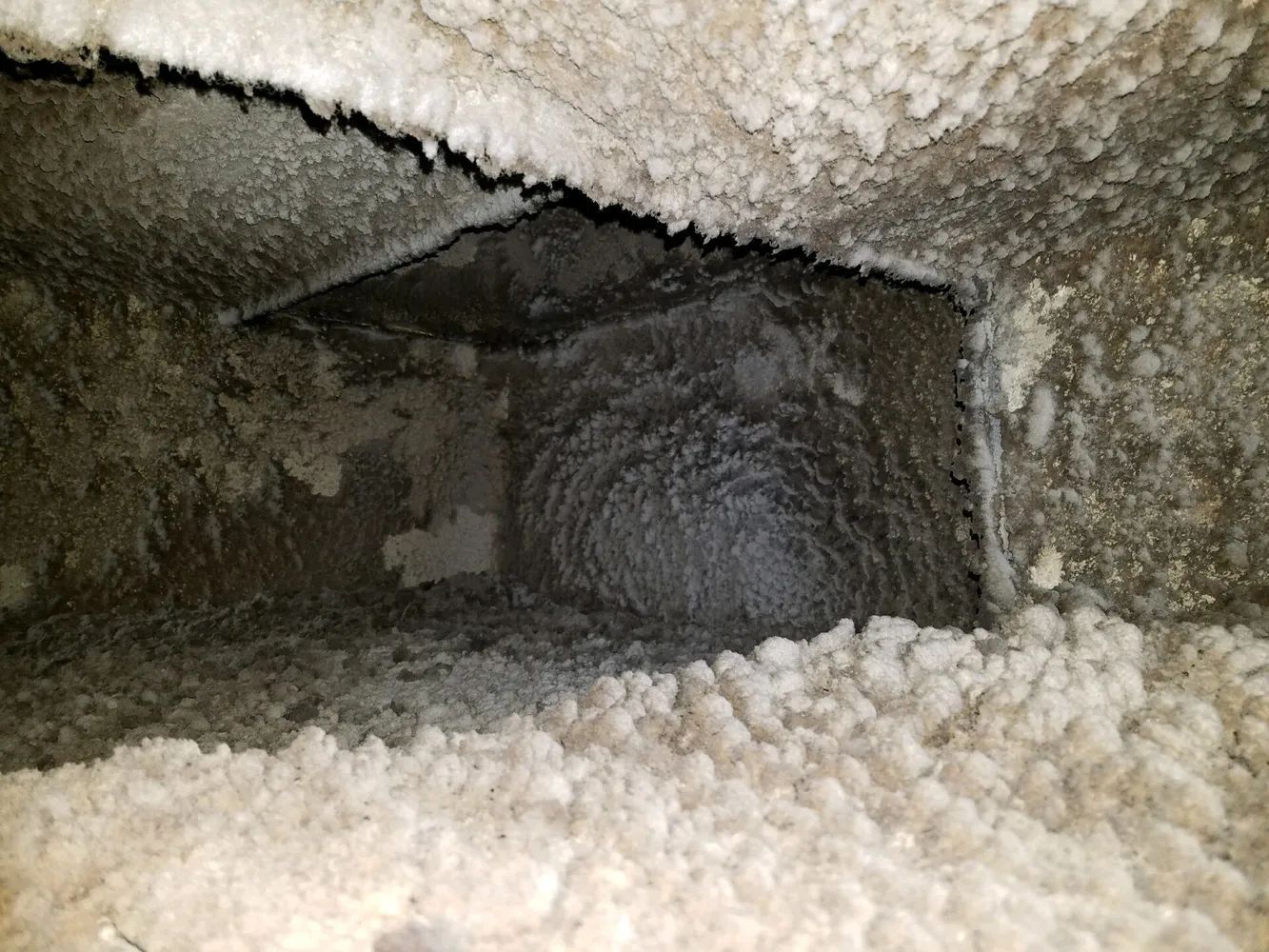 Inside a dusty air duct with fluffy white insulation along the edges