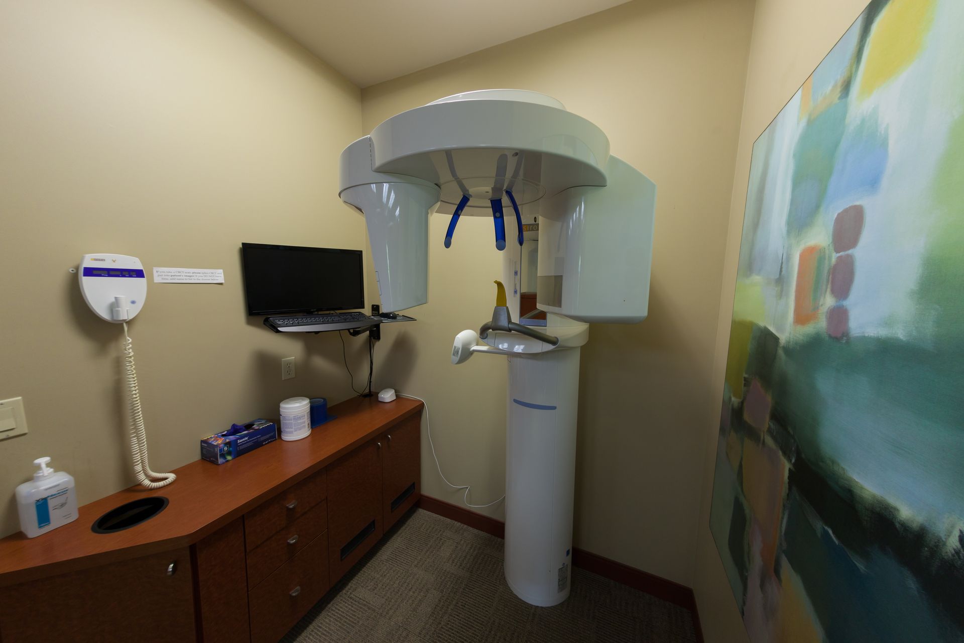 A room with a dental x-ray machine and a painting on the wall.