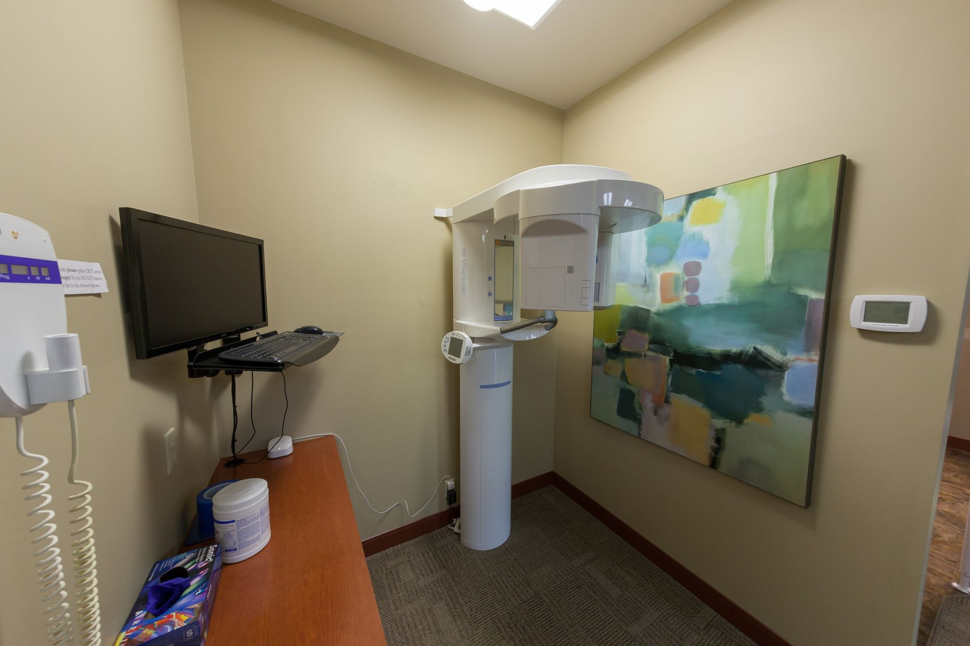 A room with a computer and a painting on the wall.