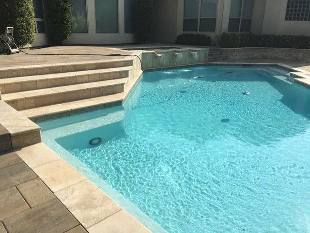 Pool with stone steps, turquoise water, and fountains; located in a sunny backyard.