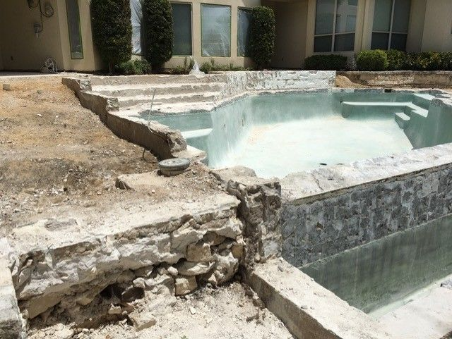 Pool undergoing renovation, concrete demolition visible, partially filled with water, outdoor setting.