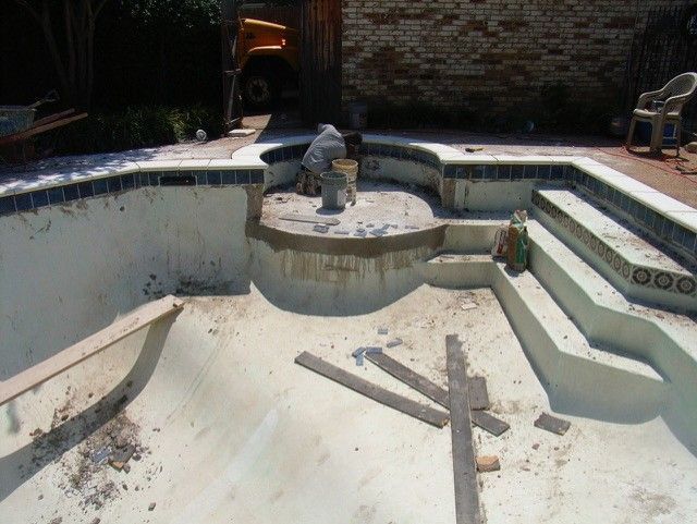 Empty swimming pool being renovated with steps, tile, and a worker present.