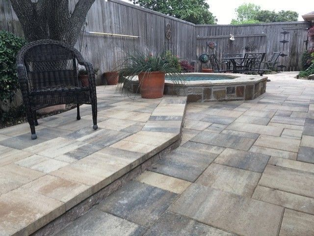Patio with stone pavers, hot tub, wicker chair, and wooden fence.