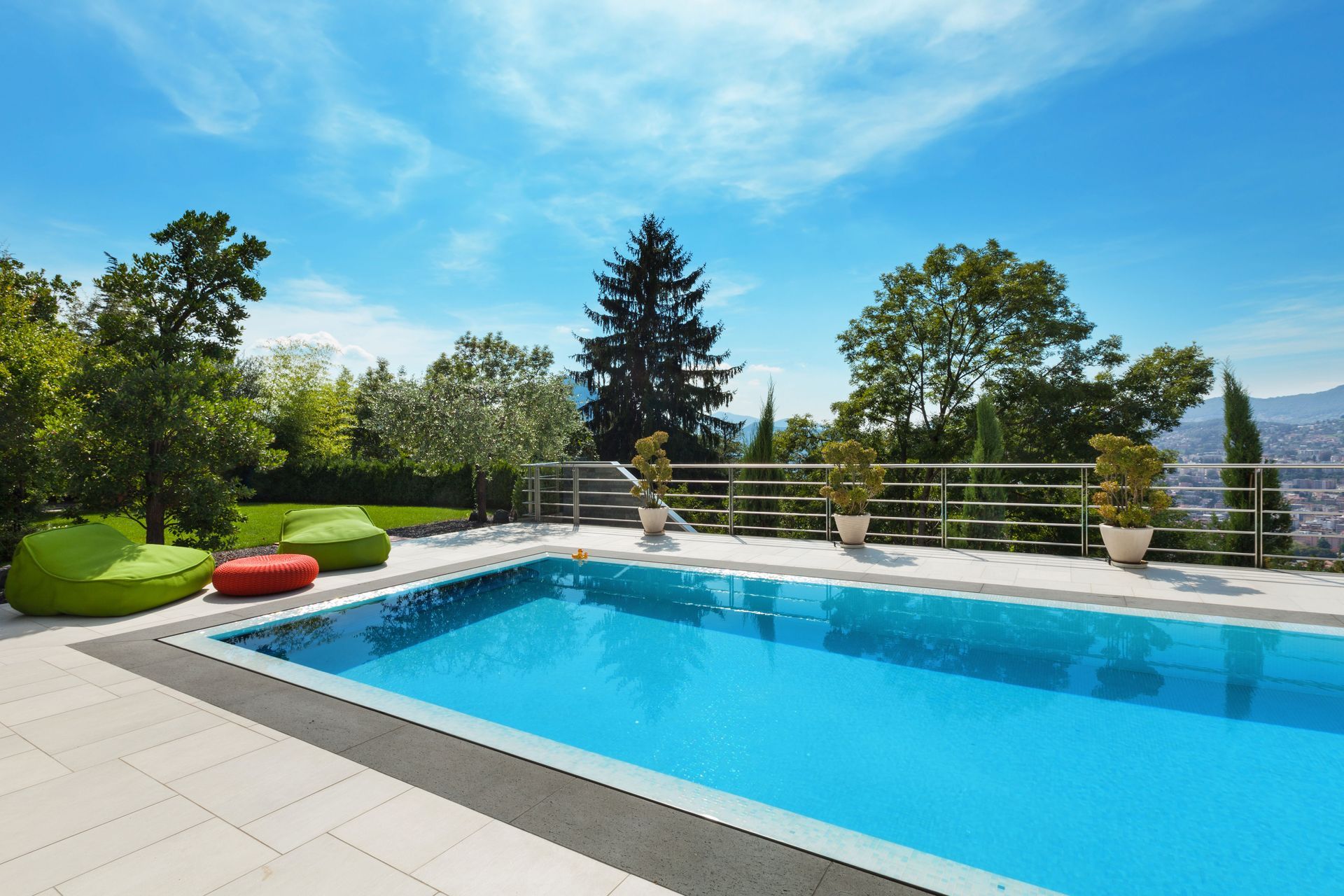 Swimming pool with blue water, lounge chairs, trees, and a scenic view under a bright blue sky.