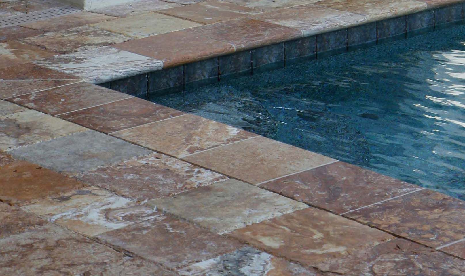 Poolside view: Multi-colored stone pavers border a swimming pool with clear blue water.
