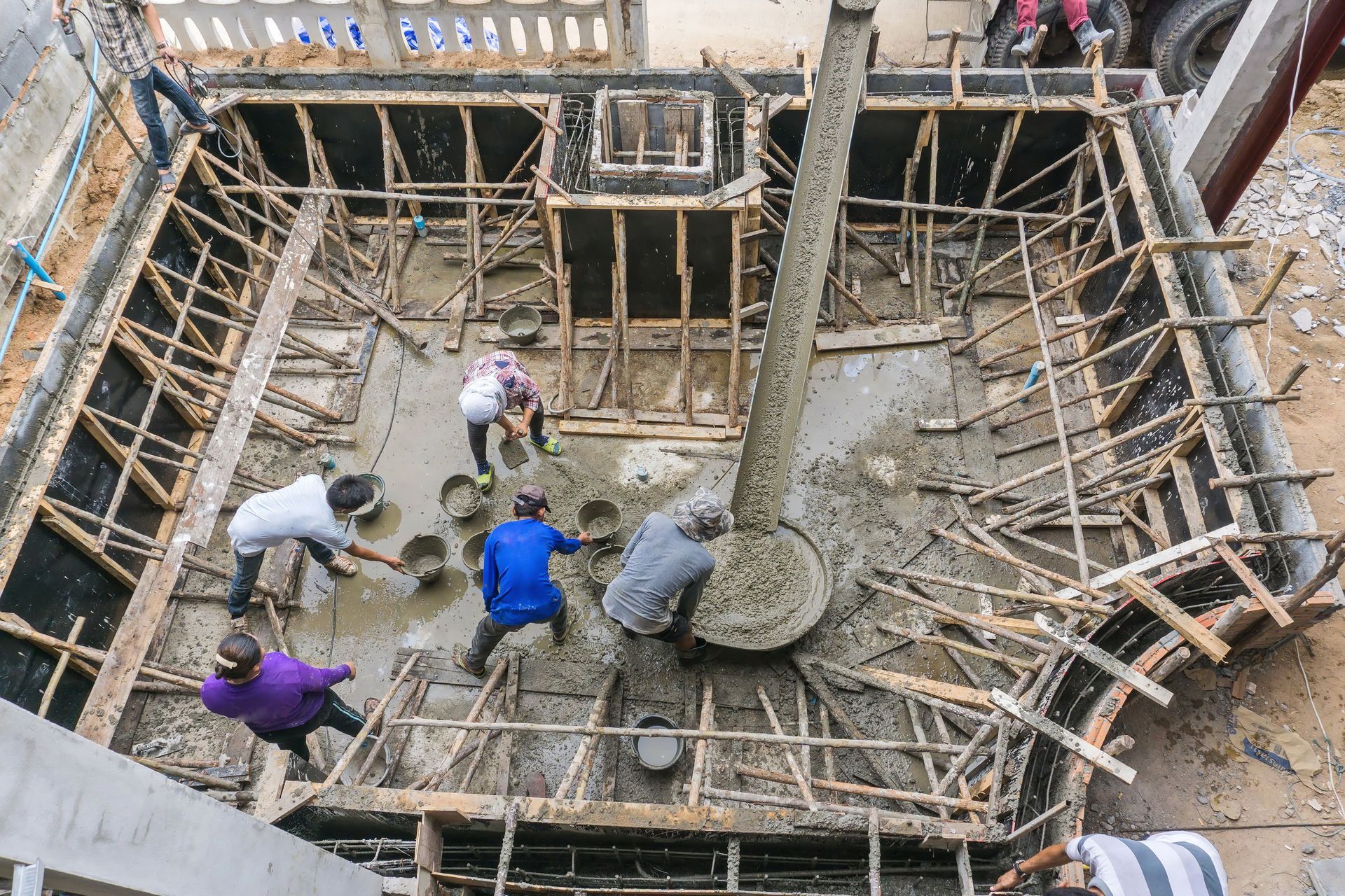 Construction workers pour concrete into a wooden frame; aerial view.