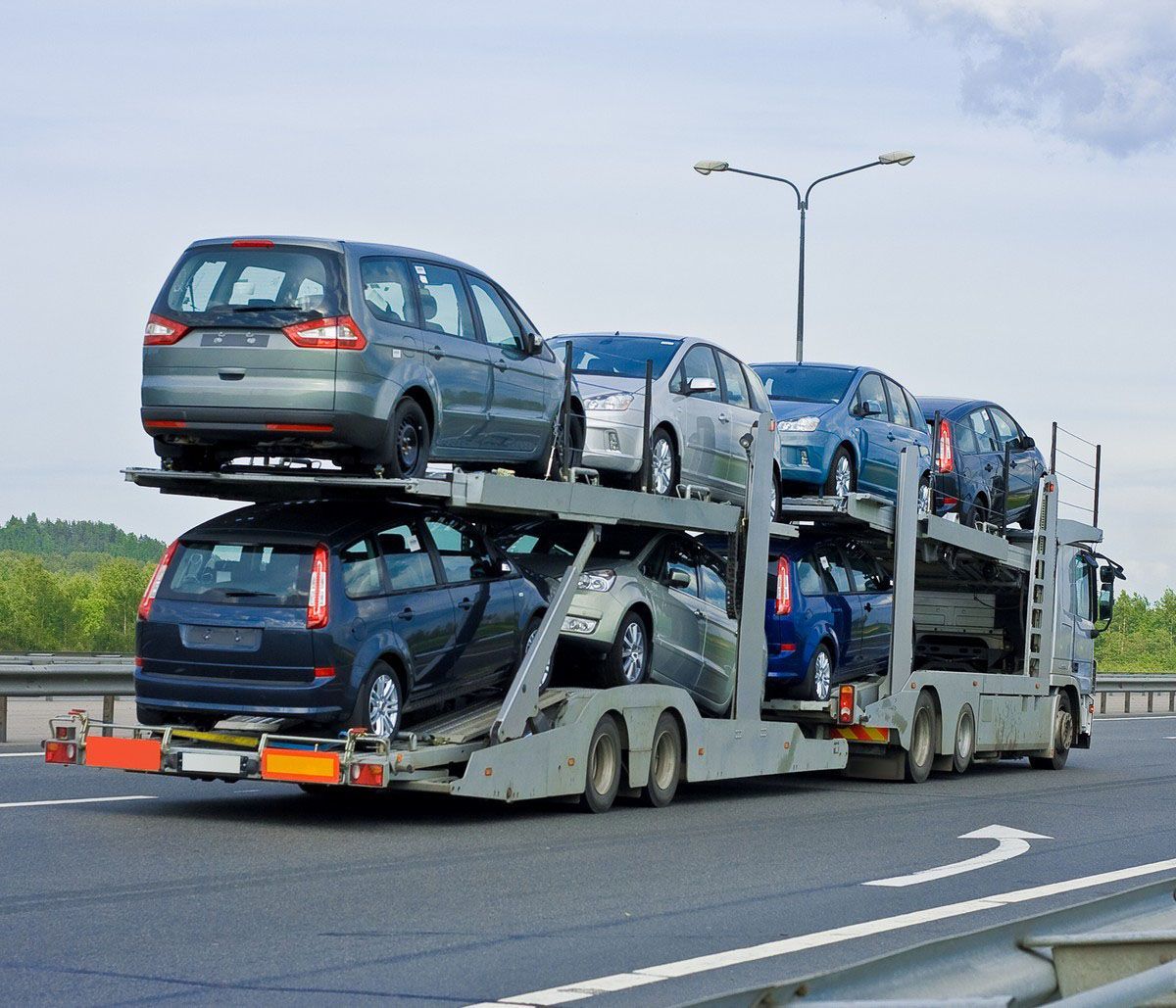 Car carrier truck transporting multiple new vehicles on a highway.