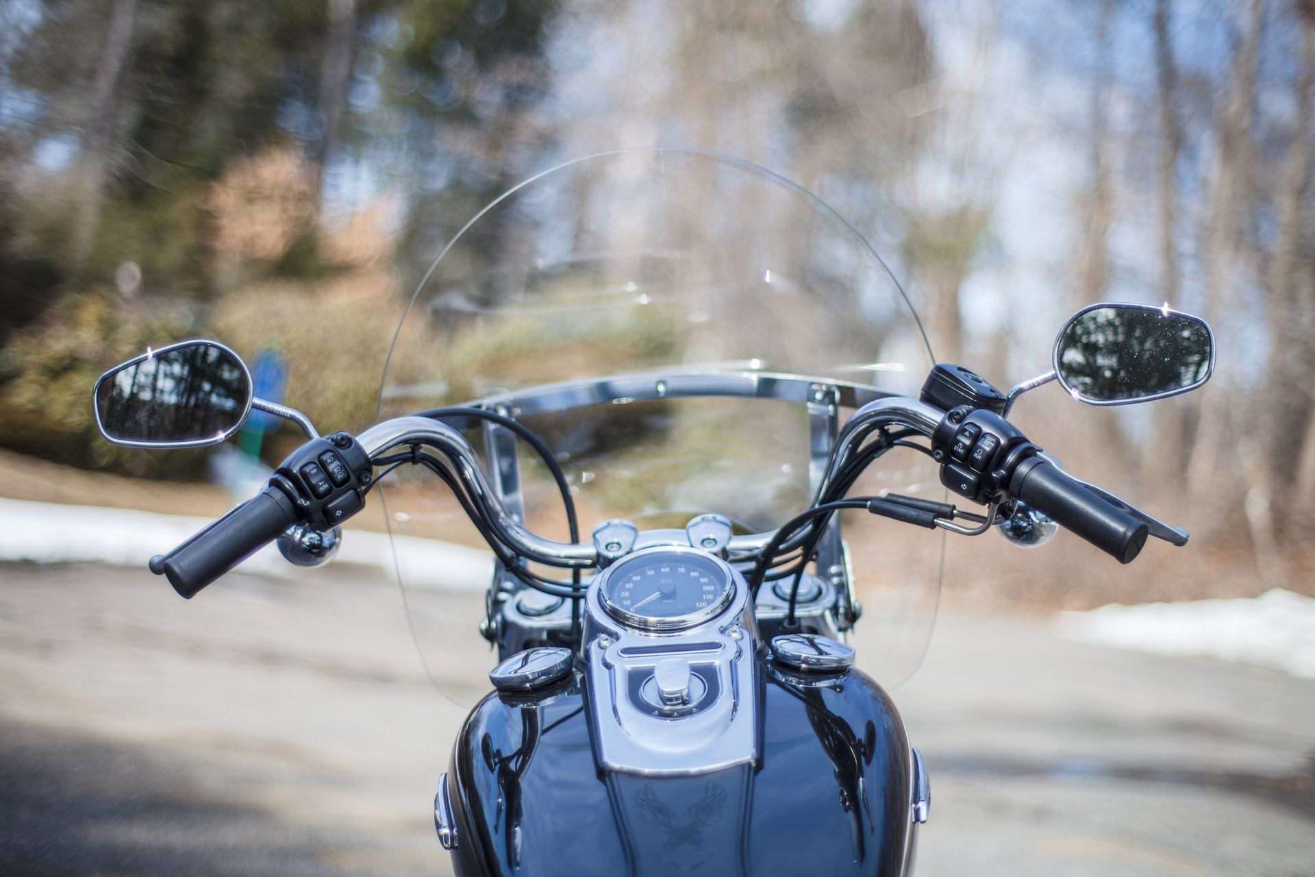 Black motorcycle handlebars with a windshield, mirrors, and a chrome speedometer.