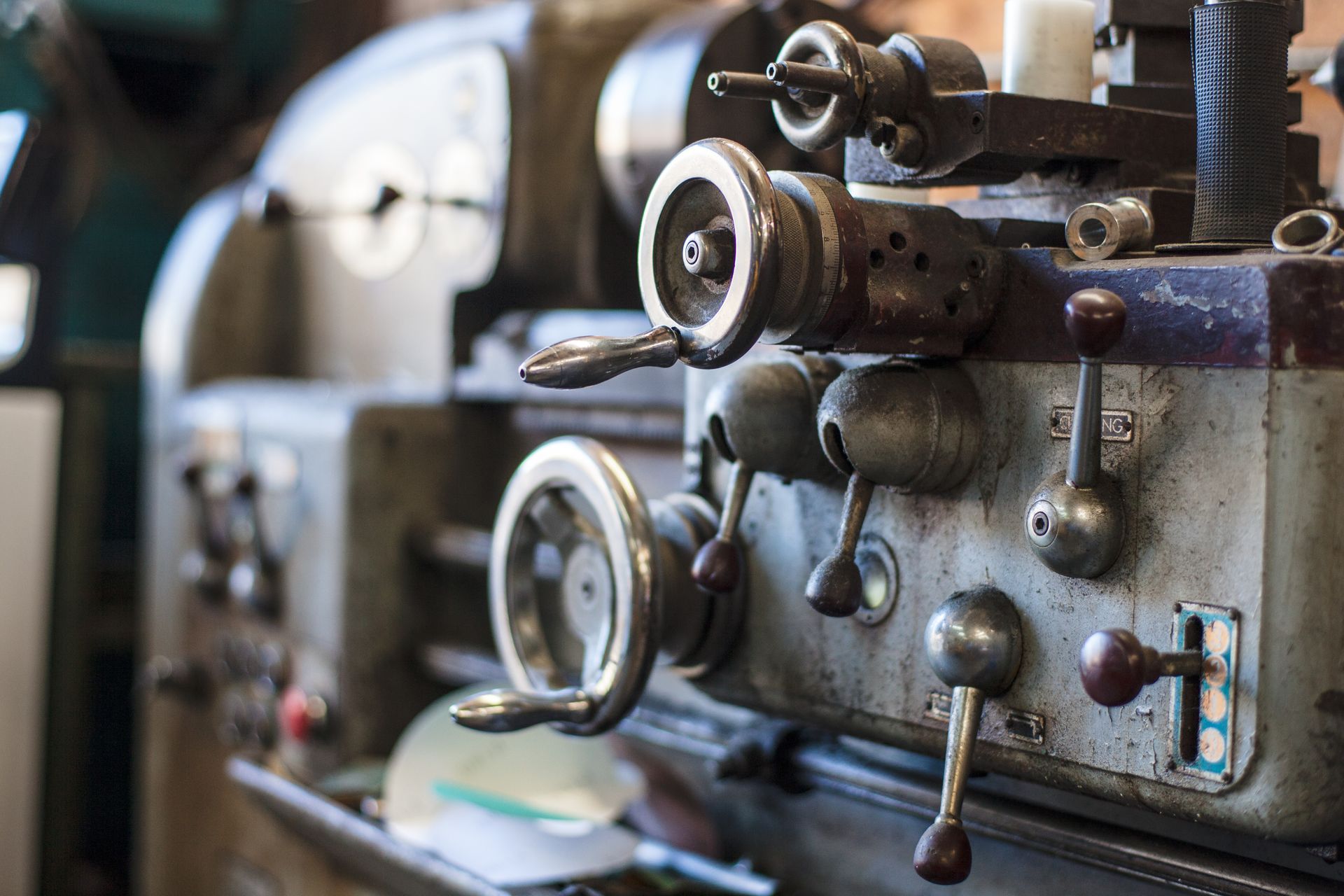 Close-up of a metal lathe machine with multiple handwheels and levers, in a workshop setting.