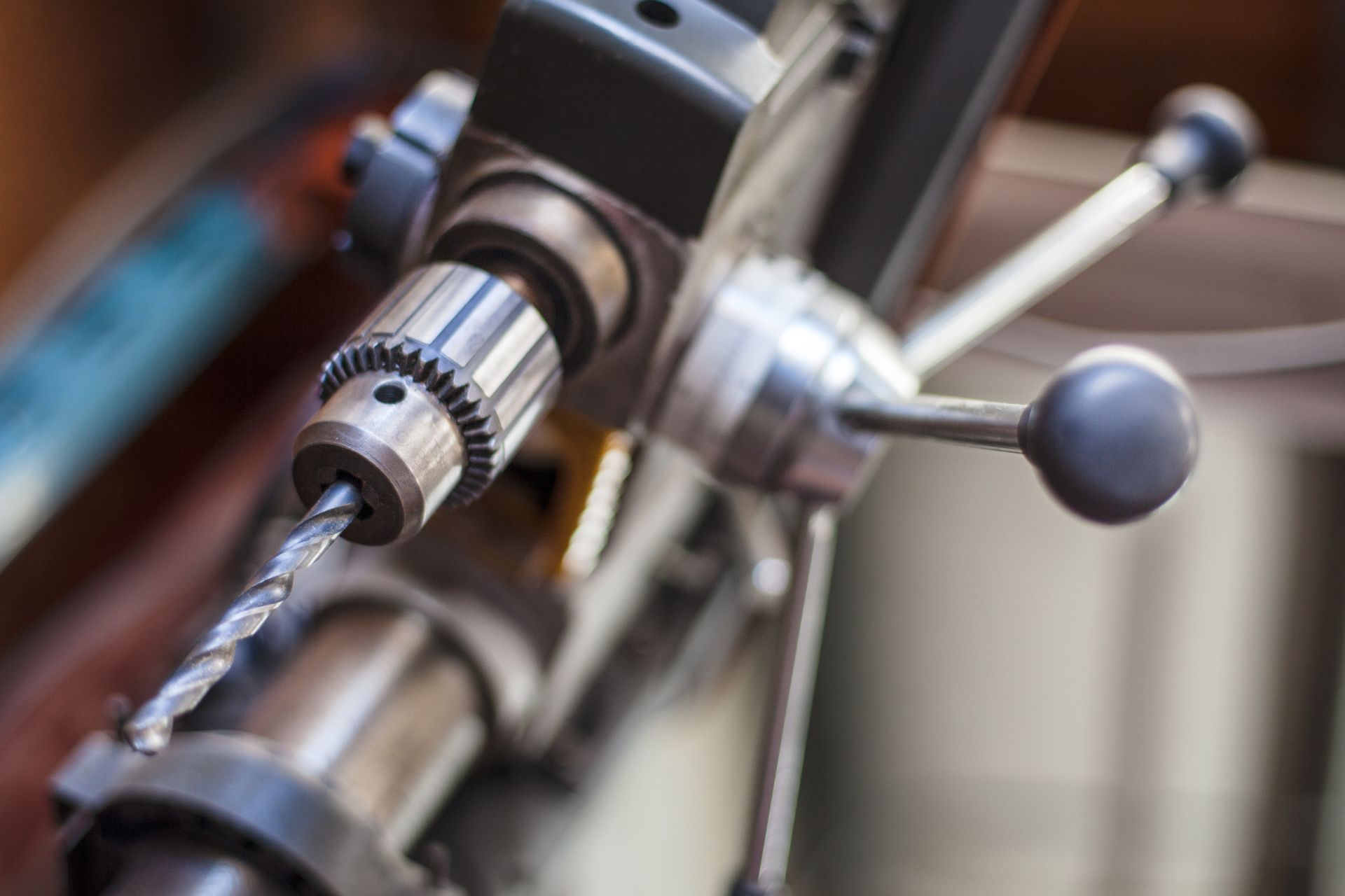 Close-up of a drill press with a drill bit in the chuck, set in a workshop.