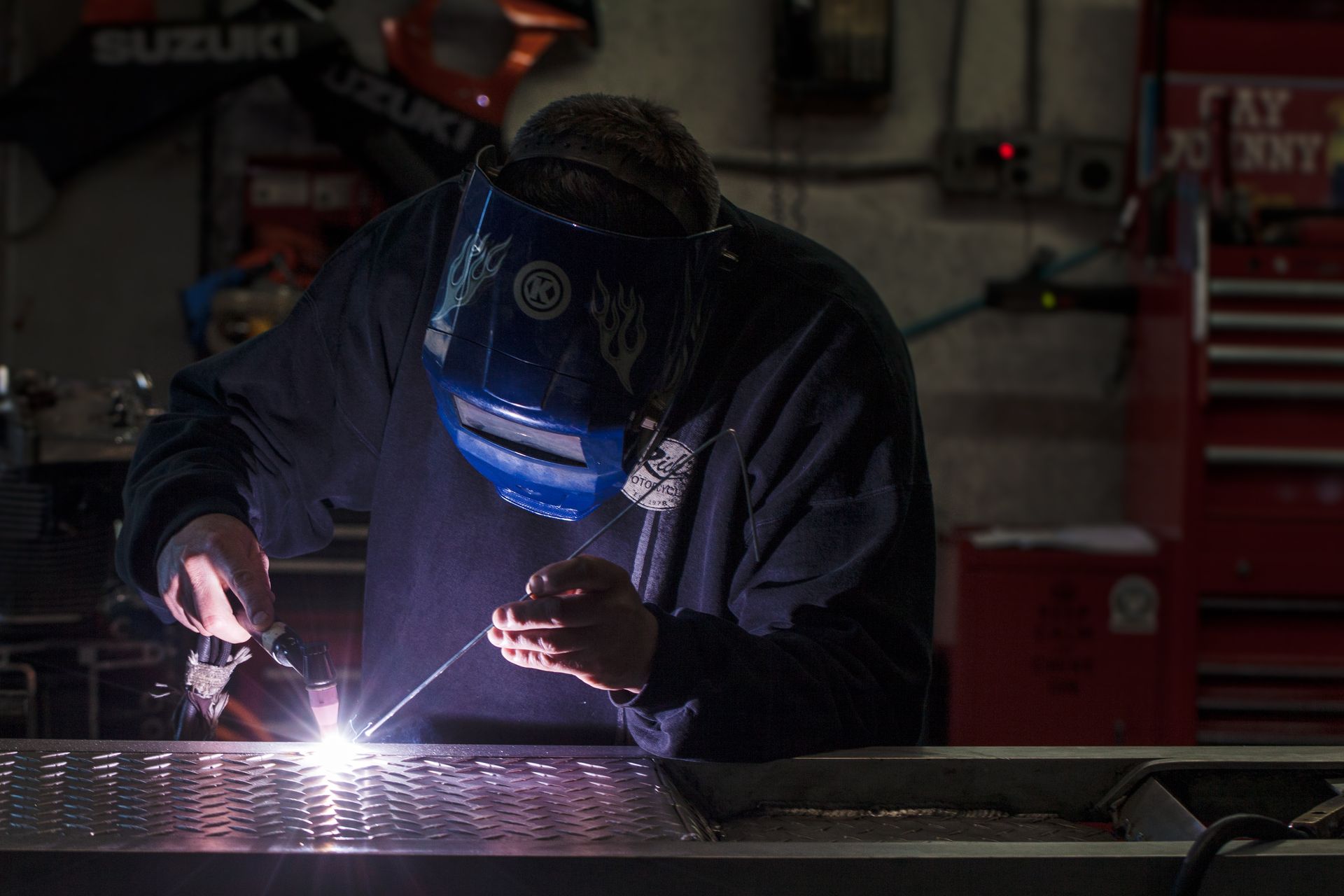 Welder in a workshop, wearing a helmet, welding on a metal surface; sparks are visible.