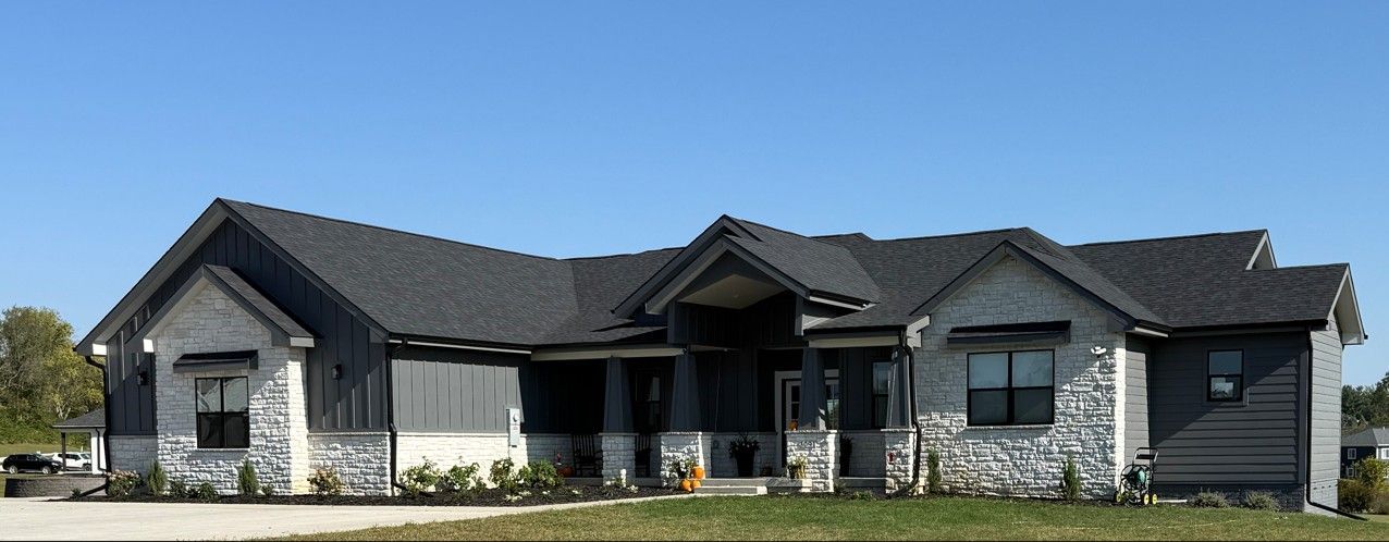 Modern house with gray and white stone exterior, dark roof, blue sky backdrop