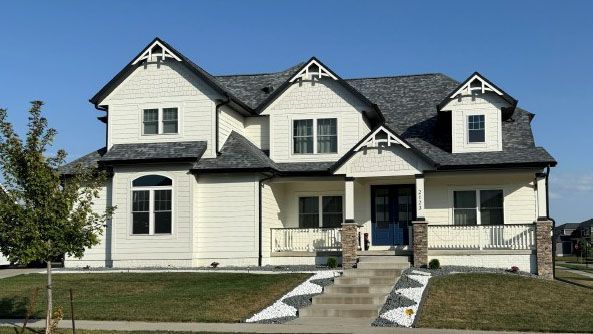Beige two-story house with gray roof, blue door, and small front porch on a sunny day