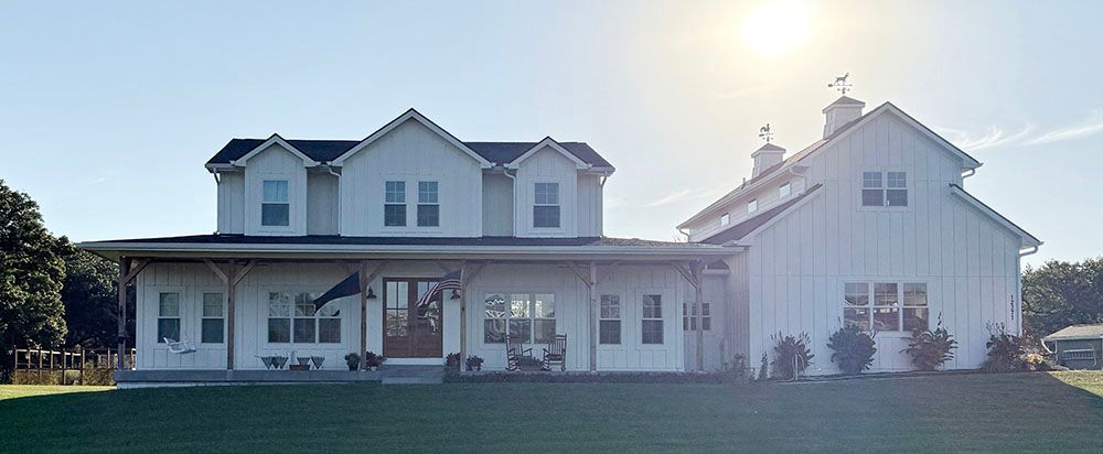 White farmhouse with a large porch and barn, bright sunlight