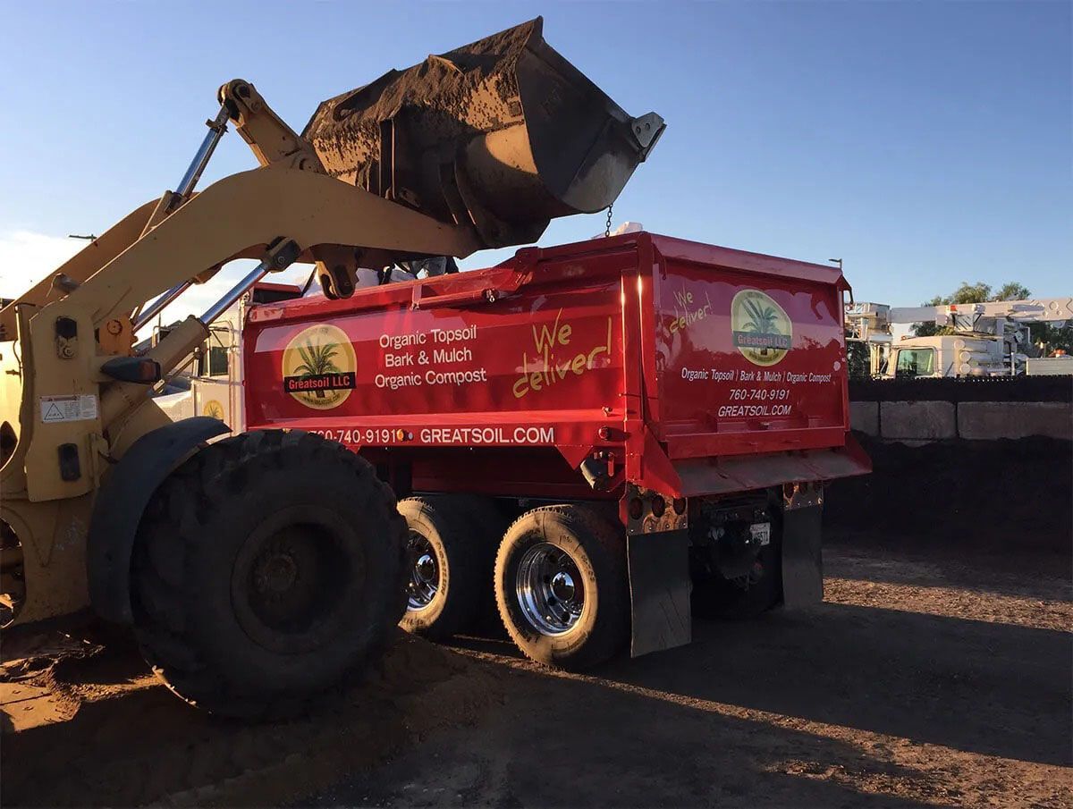 A dump truck is being loaded with dirt by a bulldozer.