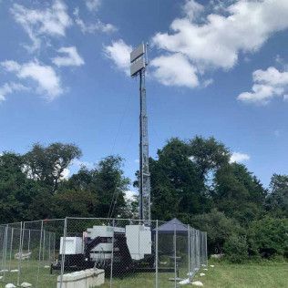 A cell phone tower is sitting in the middle of a field behind a fence.