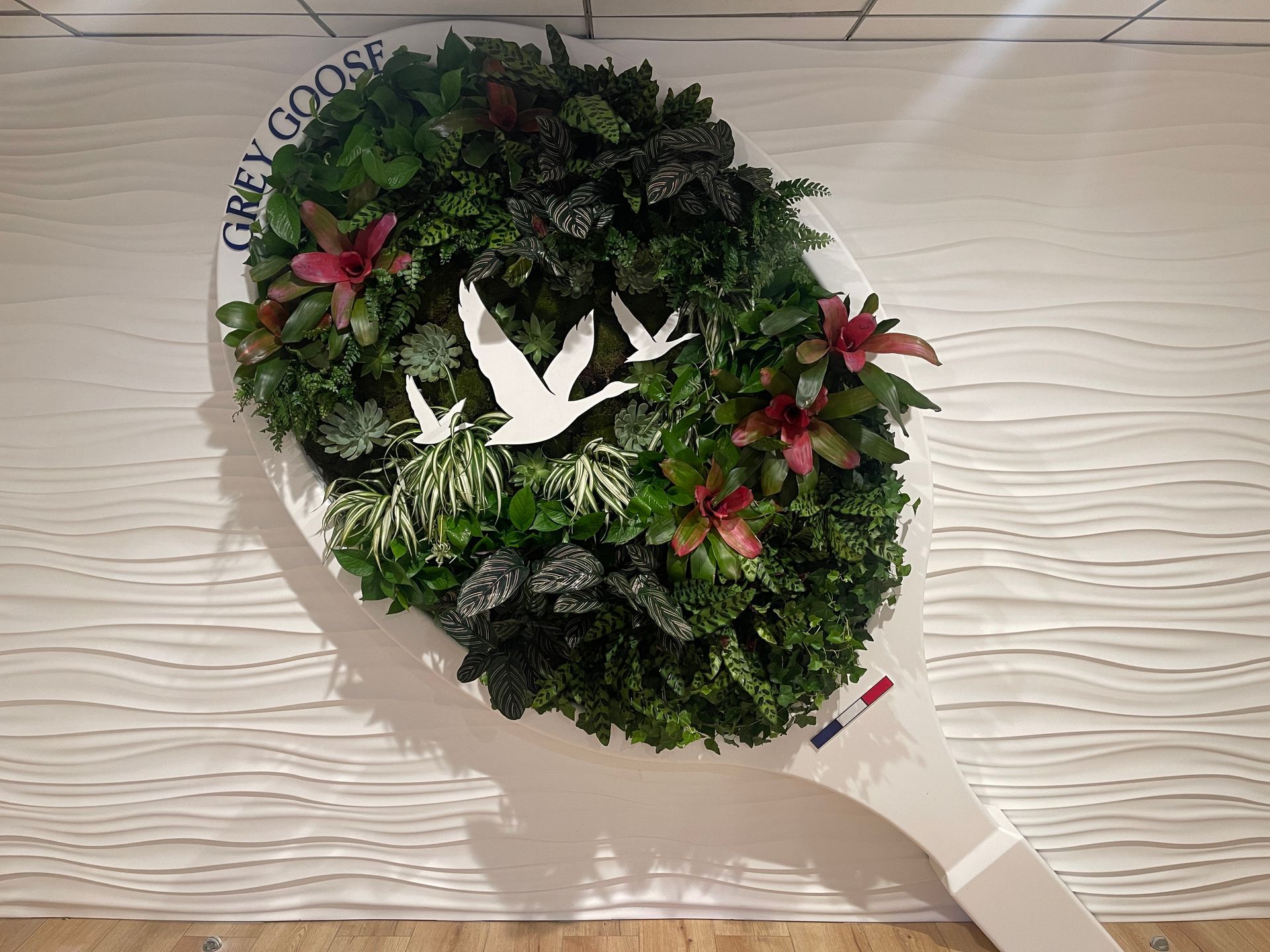 A large spoon filled with plants and birds is hanging on a wall.