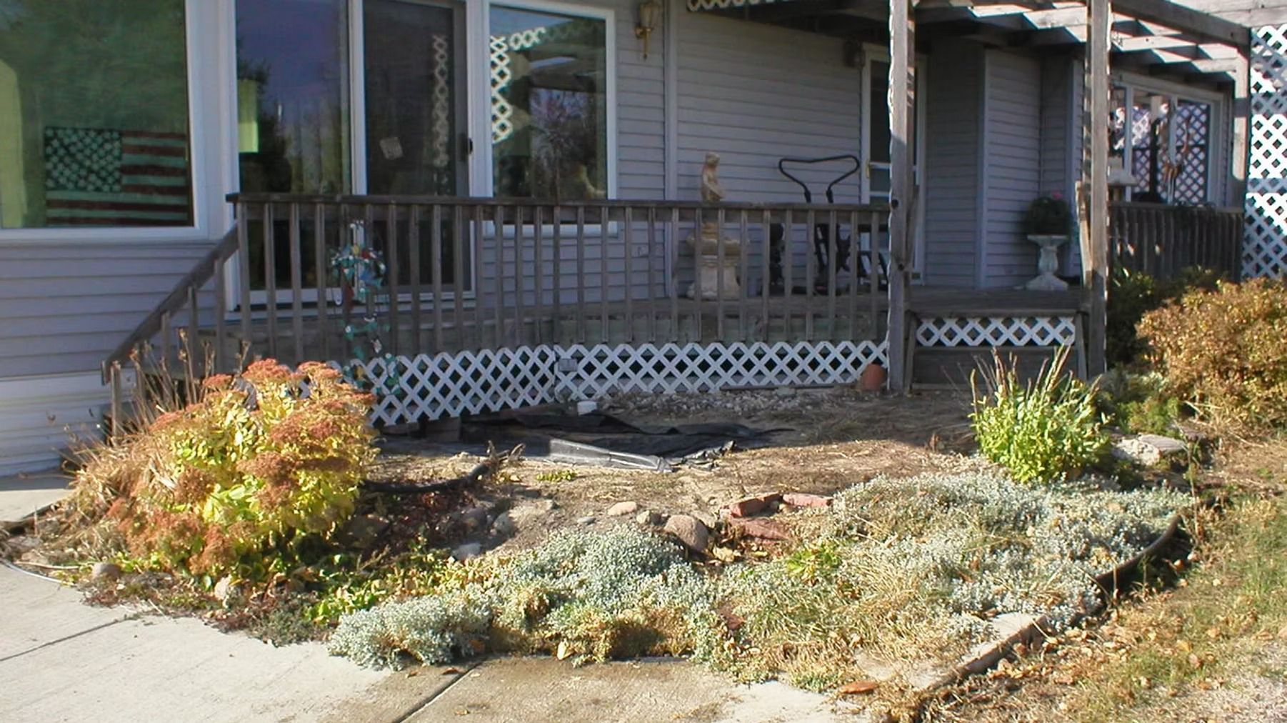 Front porch of a house with a wooden railing and garden beds in front